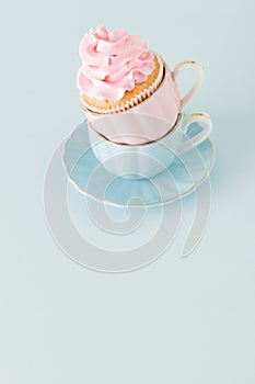 Cupcake with gentle pink cream decoration in two cups on blue pastel background.