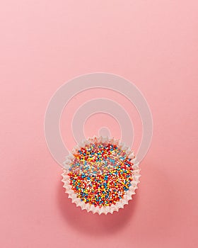 Cupcake liner with colored sugar inside at the bottom from above. Flat lay top view. Confectionery cooking concept on bright pink