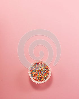 Cupcake liner with colored sugar inside at the bottom from above. Flat lay top view. Confectionery cooking concept on bright pink