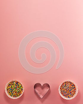 Cupcake liners with colored sugar inside and heart shaped cutter on bottom from above. Flat lay top view. Confectionery cooking