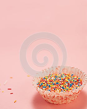 Cupcake liners with colored sugar inside and near it. Confectionery cooking concept with copy space on pink bright paper