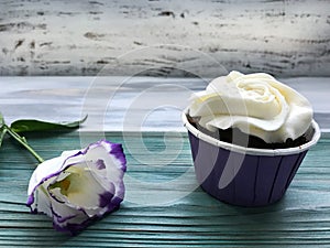 A cupcake with white cream and a flower un the wood