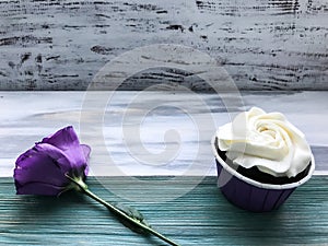 A cupcake with white cream and a flower un the wood