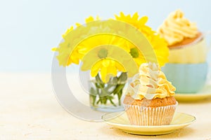 Cupcake with yellow cream decoration and bouquet of yellow chrysanthemum in glass on tender pastel background.