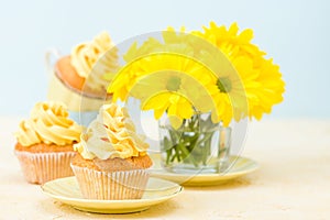 Cupcake with yellow cream decoration and bouquet of yellow chrysanthemum in glass on tender pastel background.