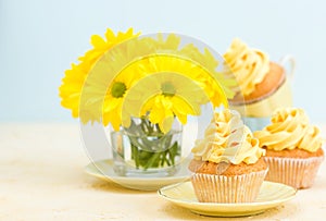 Cupcake with yellow cream decoration and bouquet of yellow chrysanthemum in glass on tender pastel background.