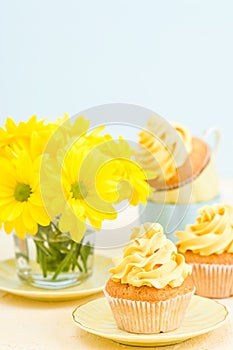 Cupcake with yellow cream decoration and bouquet of yellow chrysanthemum in glass on tender pastel background.