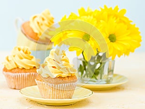 Cupcake with yellow cream decoration and bouquet of yellow chrysanthemum in glass on tender pastel background.