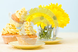 Cupcake with yellow cream decoration and bouquet of yellow chrysanthemum in glass on tender pastel background.