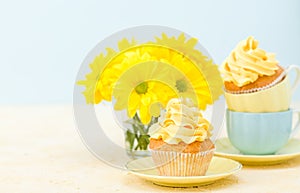 Cupcake with yellow cream decoration and bouquet of yellow chrysanthemum in glass on tender pastel background.