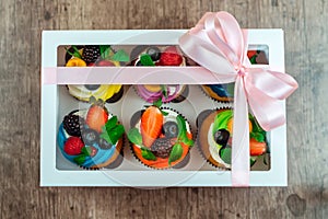 Cupcakes with berries in a gift box with a bow.