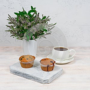 Cupcakes with black currants on a white wooden cutting board against the background of a cup of tea.