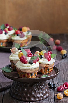 Cupcakes with butter cream and raspberry curd, decorated with berries on a wooden surface.
