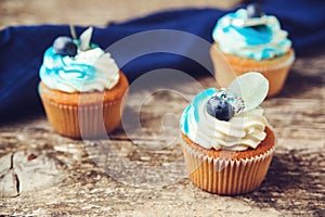 Cupcakes decorated with blue creamcheese and fresh berries. Tasty cupcakes with blueberry on wooden background. Birthday cupcakes photo