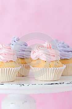 Cupcakes decorated with pink and violet buttercream on shabby shic stand on pastel pink backgroun