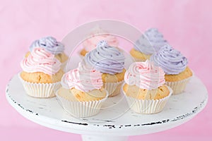 Cupcakes decorated with pink and violet cream on white shabby shic stand on pastel pink background.