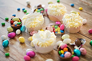 Cupcakes with easter eggs and candies on table