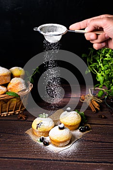 Cupcakes with mint and blackcurrant leaves in powdered sugar on a black background, a wooden basket with cupcakes and