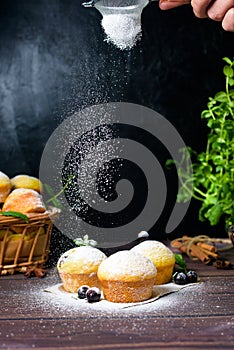Cupcakes with mint and blackcurrant leaves in powdered sugar on a black background, a wooden basket with cupcakes and