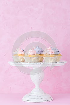 Cupcakes with pink and violet cream on white shabby shic stand on pastel pink background.