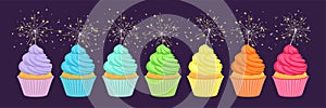 Cupcakes in rainbow colors with sparklers on dark background.