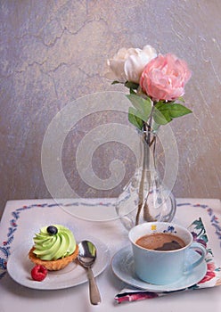 Cupcakes on a table with a cup of coffee and a vase of roses