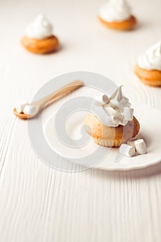 Cupcakes with vanilla cream and marshmallow on white plate, on wooden backdrop, vertical composition