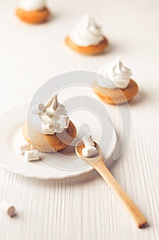 Cupcakes with vanilla cream and marshmallow on white plate, on wooden backdrop, vertical composition