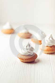 Cupcakes with vanilla cream and marshmallow on white plate, on wooden backdrop, vertical composition