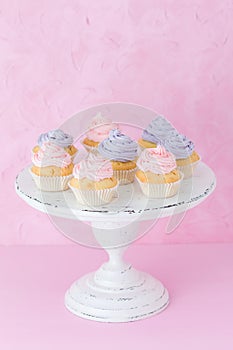 Cupcakes with violet and pink cream on white shabby shic stand on pastel pink background