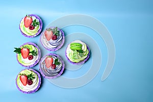 Cupcakes with whipped cream decorated chocolate bar, strawberry ,macaroons on blue background. Picture for a menu or a