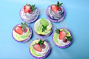 Cupcakes with whipped cream decorated chocolate bar, strawberry ,macaroons on blue background. Picture for a menu or a