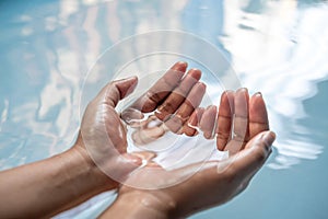 Cupped hands partially submerged in clear blue drinking water - Wet hands raised from a fresh water spring