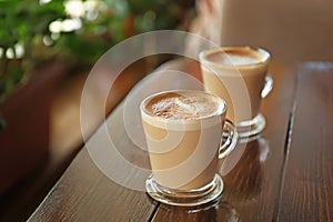 Cups of aromatic coffee with foam on wooden table