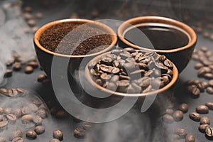 Cups of coffee among selected and calibrated Arabica coffee beans scattered on a black background.