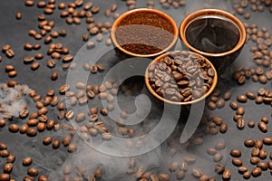 Cups of coffee among selected and calibrated Arabica coffee beans scattered on a black background.