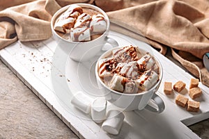 Cups of delicious cocoa drink with marshmallows on wooden board