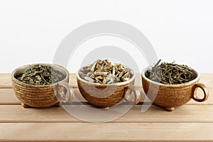 Cups with green and white tea leaves on a white background