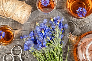 Cups of herbal tea, transparent teapot and blue cornflowers flowers on wood background. Top view Flat lay