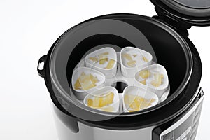 Cups of pineapple yogurt in multi cooker on white, closeup