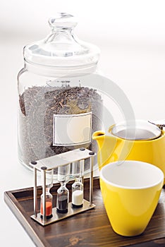 Cups and teapot set with watches and loose tea in a container on white background, product for tearoom on wooden plate