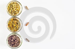 Curative herbs in glass jars and capsules on a white background