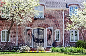 Curb appeal-Pretty upscale two story brick house with arched door and shtters and dogwood trees in bloom