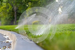 Curb of the paved road with water sprinklers on the vivid green grassy roadside