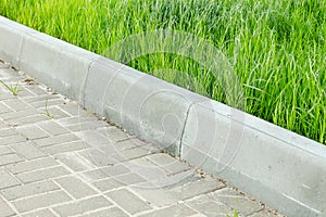 A curbstone separates the pedestrian zone from the green tall grass of the lawn. City improvement