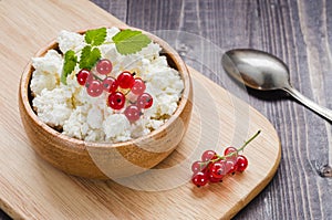 curd cheese with red currant in a wooden plate/curd cheese with red currant in a wooden plate on a dark background. Top view