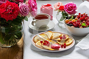 Curd pancakes with berry curd served with tea on a table decorated with bouquets of roses