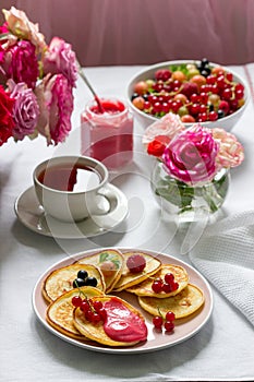 Curd pancakes with berry curd served with tea on a table decorated with bouquets of roses.