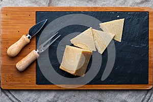 Cured sheep cheese. Cut into pieces on wooden board and black slate. Fork and knife for cheese. Top View