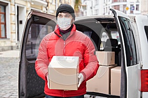 Curier in medical mask holding cardboard box